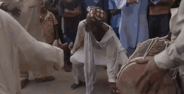 a man in a white shirt is kneeling down in front of a drum in a crowd .