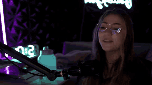 a woman wearing glasses stands in front of a microphone with the word good above her