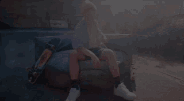 a man in a purple shirt is sitting on a couch with a skateboard .