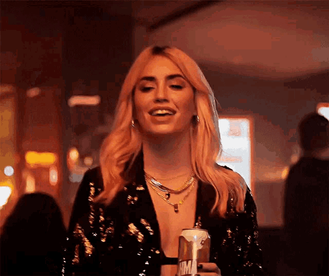 a woman in a black sequined top is holding a can of soda