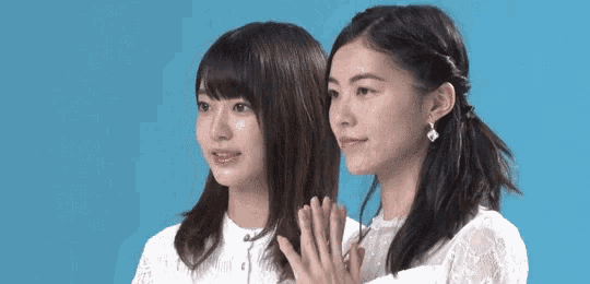 two young women are standing next to each other on a blue background and looking at each other .