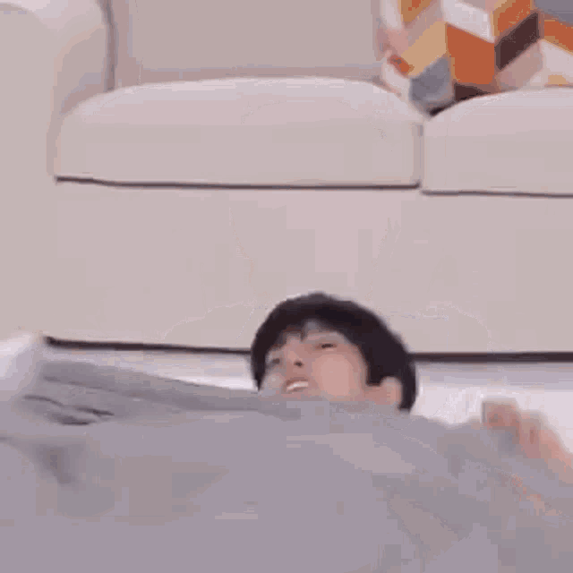 a young boy is laying on a bed with a blanket on his head .
