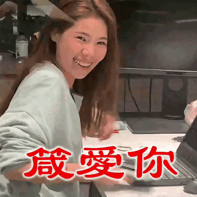 a woman is smiling in front of a laptop with chinese writing on the screen