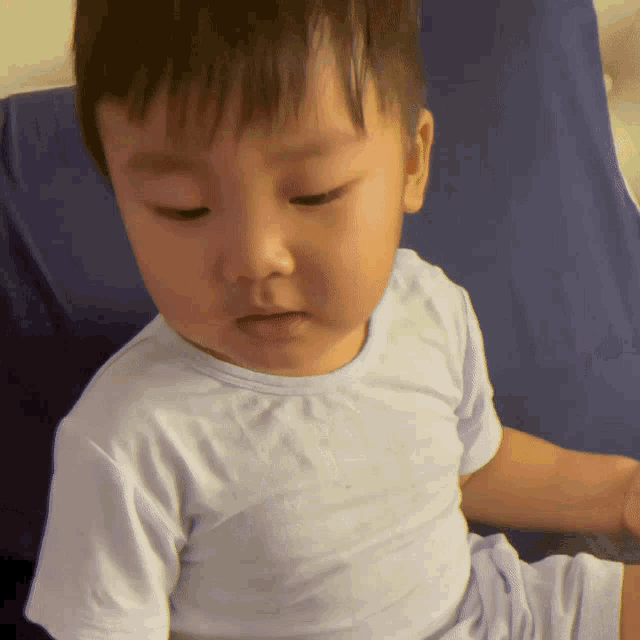 a baby in a white shirt looks down at something