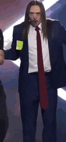 a man with long hair is wearing a suit and tie and has a name tag on his chest