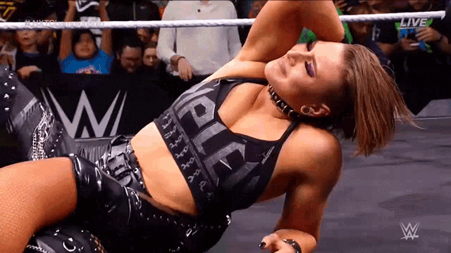 a female wrestler is laying on the ground in a wrestling ring while a crowd watches .