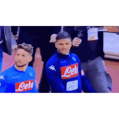a man in a blue shirt with the word napoli on it is standing next to another man .