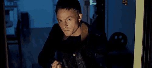 a man is holding a gun in a dark room and looking out a window .