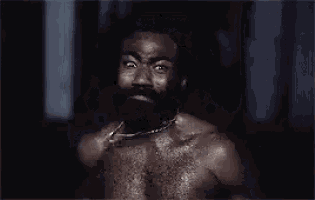 a shirtless man with a beard and a chain around his neck is making a funny face .