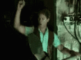 a man in a blue shirt is standing in a dark room with his arm in the air .