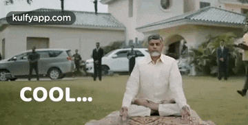 a man with a beard is sitting in a lotus position on a rug in front of a house .