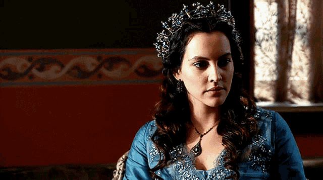 a woman wearing a blue dress and a tiara is sitting in front of a window .