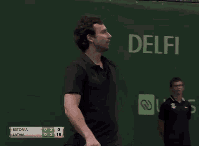 a man is holding a tennis racquet in front of a scoreboard that says estonia and latvia