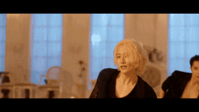 a man with blonde hair is dancing in a room with a lot of windows