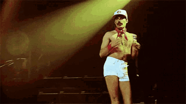 a man without a shirt is dancing on a stage while wearing shorts and a hat .