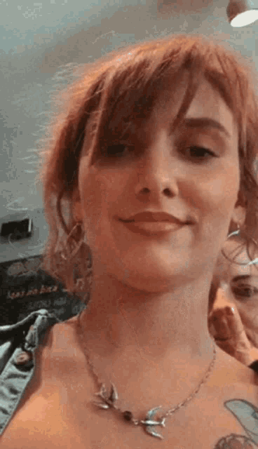 a woman wearing a necklace with a bird on it smiles for the camera