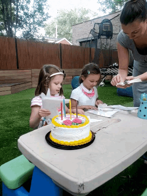 two little girls sitting at a table with a birthday cake and candles