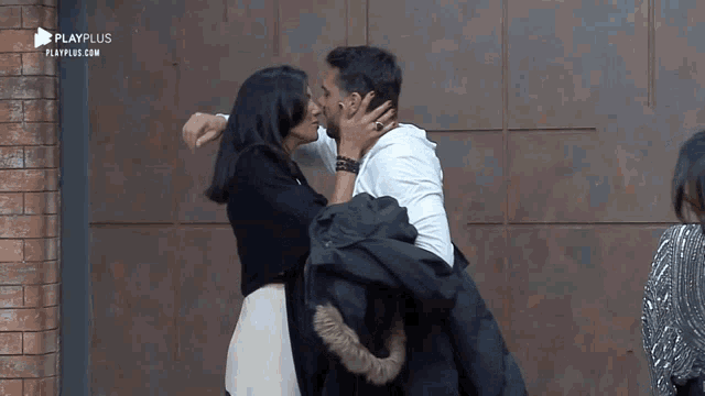 a man and woman kissing in front of a playplus sign