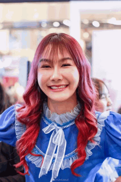 a woman with red hair is smiling and wearing a blue shirt with ruffles