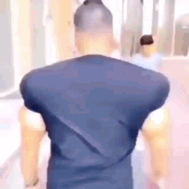 a man in a blue shirt is walking down a hallway with his back to the camera .