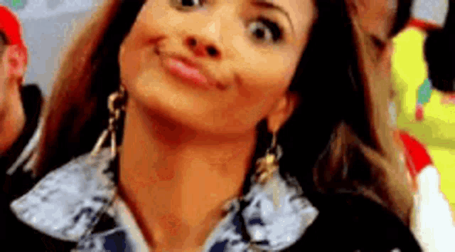 a woman wearing earrings and a ruffled shirt is smiling and making a funny face .