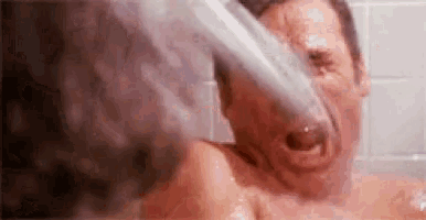 a man is taking a shower with a shower head in his face .