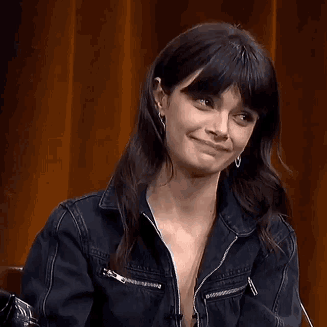 a woman wearing a denim jacket and earrings laughs
