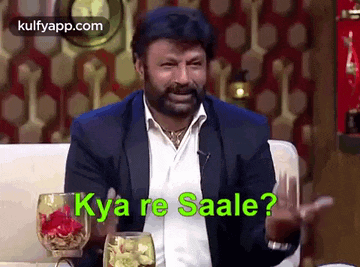 a man in a suit is sitting on a couch with a glass of wine and says kya re saale ?