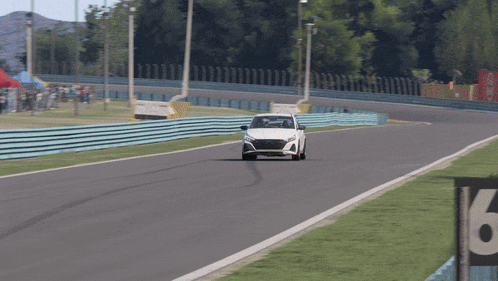 a white car is driving down a race track with a fence in the background