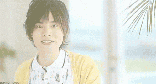 a young man wearing a yellow cardigan and a white shirt is smiling in front of a window .