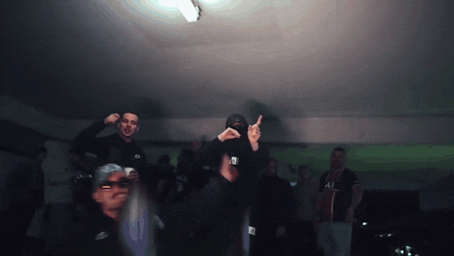 a group of people are standing in a dark room and one of them is wearing a shirt that says " all "