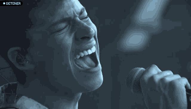 a close up of a man singing into a microphone with the word detener above him