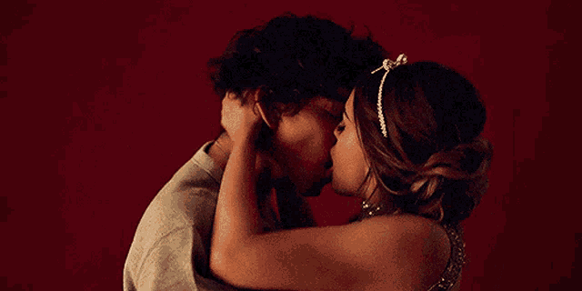 a boy and a girl are kissing in front of a red background .