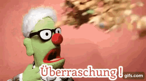 a green puppet with glasses and a red nose is blowing a bunch of confetti ..