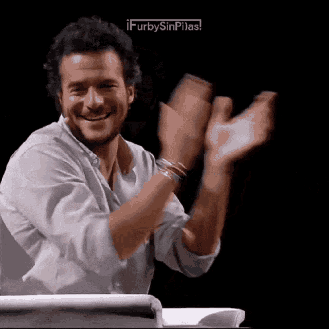 a man in a white shirt is clapping his hands in front of a black background