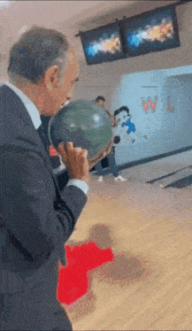 a man in a suit is holding a bowling ball in a bowling alley with the letters w and l on the wall