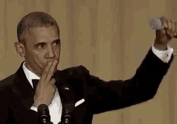 barack obama is giving a speech in front of a microphone while covering his mouth with his hand .