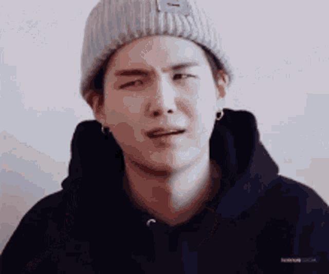 a young man wearing a beanie and a hoodie is crying .