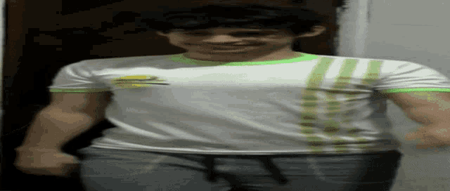 a young man wearing a white shirt with green stripes on the sleeves is smiling