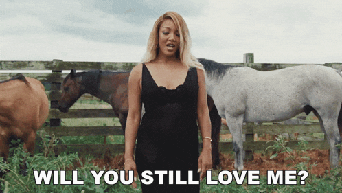 a woman in a black dress is standing in a field with horses and the words will you still love me