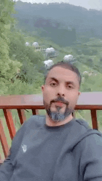 a man with a beard is making a peace sign while sitting on a balcony .