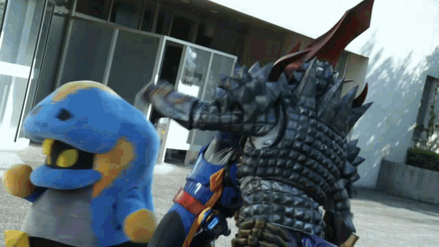 two monsters are standing in front of a building and one has spikes on his back