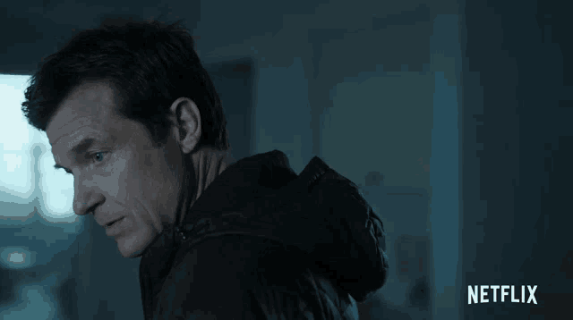 a man in a black jacket stands in a dark room with netflix written on the bottom