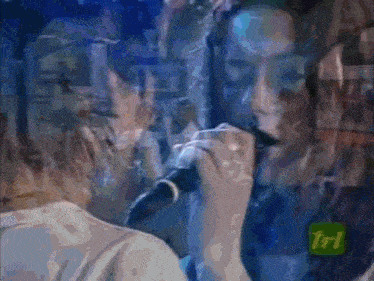 a woman singing into a microphone with a tri logo on the bottom left