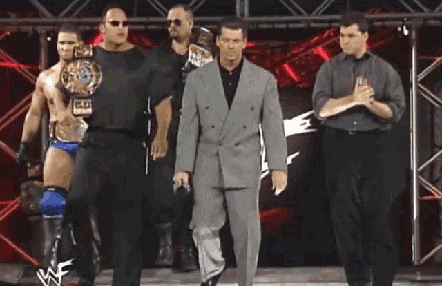 a group of wrestlers are walking on a stage with one holding a world heavyweight wrestling championship belt