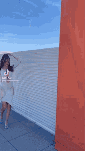 a woman in a white dress is holding a blue purse while leaning against a wall .