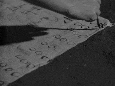 a black and white photo of a person writing on a piece of paper with numbers and letters