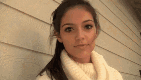 a woman wearing a white sweater and scarf is standing in front of a white wall
