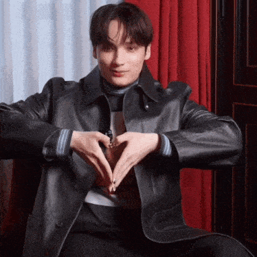 a young man in a black leather jacket making a heart shape with his hands