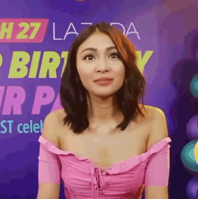 a woman in a pink off the shoulder top is standing in front of a sign that says birthday .